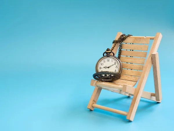 Pocket watch on the wooden beach chair on blue background (isolated). copy space for text and content. concept of vercation time and relax time.