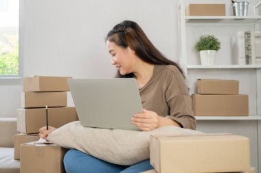Genç girişimci, kanepede oturuyor ve evde çalışıyor. Müşterilerin siparişlerini dizüstü bilgisayarla kontrol etmek ve müşteri adreslerini yazmak internet üzerinden sevkiyat yapmak. Küçük işletme sahibi kavramı.