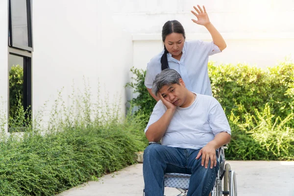Żona pchała wózek inwalidzki dla męża. Z jej ra — Zdjęcie stockowe