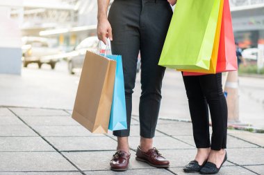 Alışveriş caddesinde yürüyen ve ellerinde renkli alışveriş torbaları tutan mutlu genç çiftler. Satış ve Kara Cuma alışverişi kavramı