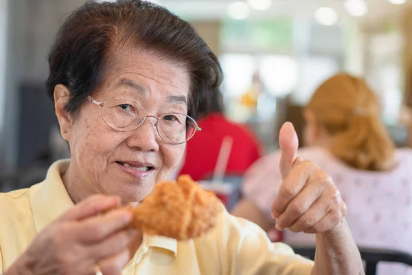 Азиатские пожилые женщины едят жареную курицу. В ресторане — стоковое фото