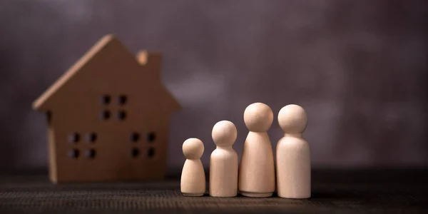Wooden figures family standing in front of a wooden house. The concept of Protection and safety, Home Security, property insurance and house.