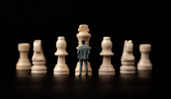 Фігури бізнесмен стоїть перед дерев'яними шахами на чорному — стокове фото