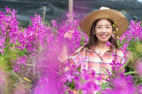 young female gardeners wear a plaid shirt and wear a hat. Hands holding scissors for cutting orchids and smile. new generation farmer, gardeners concept.