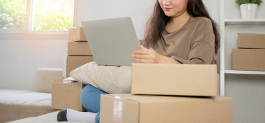 Genç girişimci, kanepede oturuyor ve evde çalışıyor. Müşterilerin siparişlerini dizüstü bilgisayarla kontrol etmek ve müşteri adreslerini yazmak internet üzerinden sevkiyat yapmak. Küçük işletme sahibi kavramı.