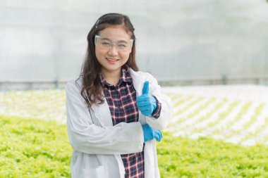 Tarım Mühendisi ayakta duruyor ve hidroponik serada gülümsüyor. Her test bitkisi sisteminde ve hasattan önce organik sebzelerin büyümesini ölçüyor. Tarım teknolojisi kavramı