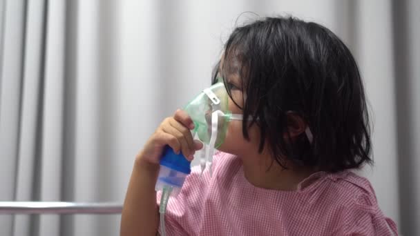 En liten asiatisk tjej som har syrgasmask och andas genom en nebulisator på sjukhuset. Begreppet bronkit, respiratorisk och medicinsk behandling. — Stockvideo