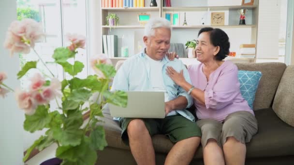Glückliches asiatisches Paar auf dem Sofa sitzend und mit einem Laptop im Internet surfen und VIDEO-Konferenz mit Familie. Konzept der Familienzusammenführung, soziale Distanzierung — Stockvideo