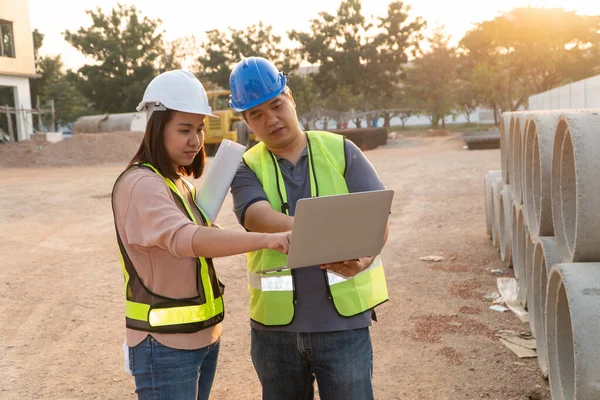 Asian woman construction engineers are checking construction specifications in laptops with technical engineers, Building Location on the background, Concept of Equality and success.