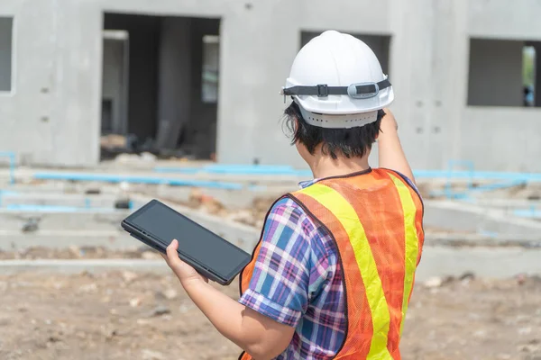 Portrait of Asian woman construction engineer worker with helmet on head using tablet while standing on construction site. building site place on background. Construction concept