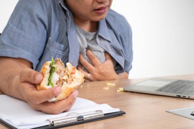 Ofis masasında çalışan ve hamburger yiyen Asyalı bir adam ve kalp krizi. Meşgul bir iş adamı kavramı sol dengede çalışamaz ve sağlıkla ilgilenmez. Sadece abur cubur yer.