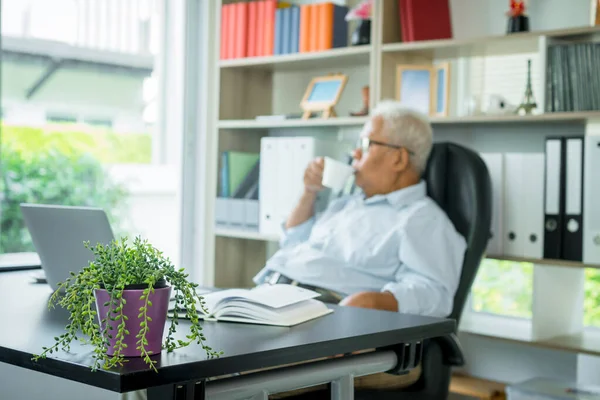 Asian elderly man sitting in front of a laptop computer, He is sitting back in his chair and relax. The elderly can still work And create sentences for society, virus quarantine,