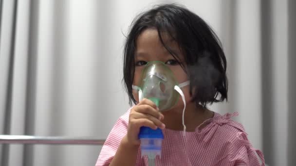 Niña asiática que tiene una máscara de oxígeno y respira a través de un nebulizador en el hospital. Concepto de bronquitis, tratamiento respiratorio y médico. — Vídeos de Stock