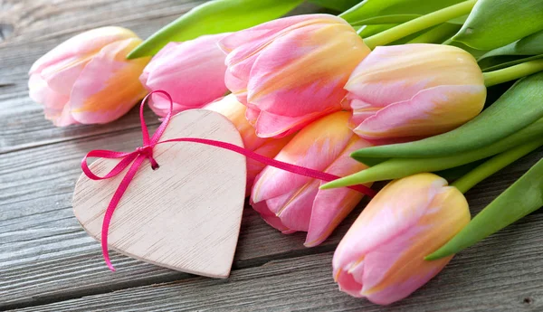 Colorful tulips and heart on wooden background