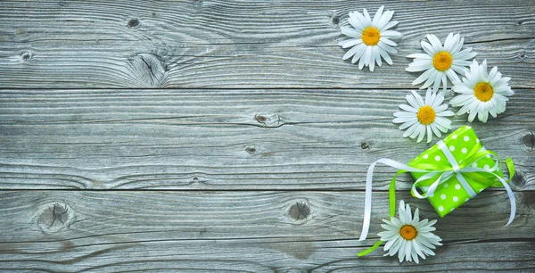 Gift box and daisy flowers on old wooden planks — Stock Photo, Image