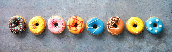 Vários donuts coloridos em uma fileira no fundo rústico — Fotografia de Stock