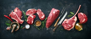 Variety of raw beef meat steaks for grilling with seasoning and utensils on dark rustic board clipart