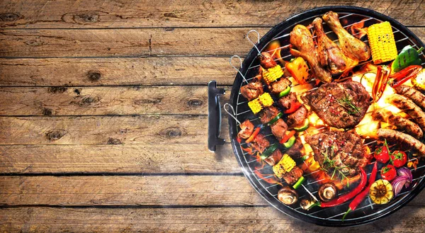 バーベキューグリルの上に煙と素朴な木製の板に炎で野菜と各種おいしいグリル肉のトップビュー — ストック写真