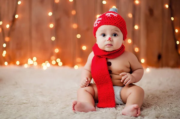 kırmızı bir Noel şapkalı küçük çocuk beyaz kürk halı üzerinde yatıyor