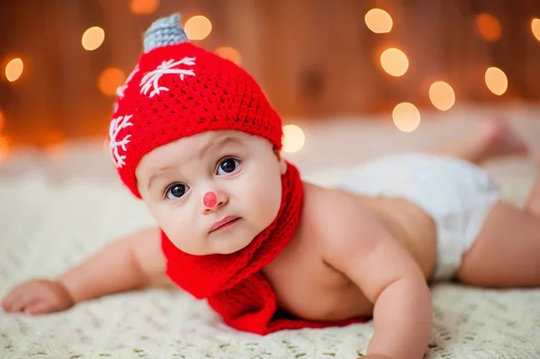 Menino em um chapéu de Natal vermelho jaz em um tapete de pele branca — Fotografia de Stock