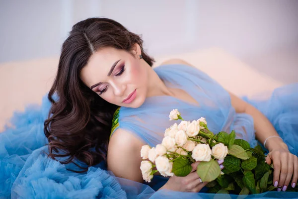 Hermosa chica con el pelo oscuro con flores en las manos en un blu — Foto de Stock