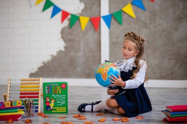 Okul üniformalı küçük bir kız elinde küre ve kitaplarla oturuyor.