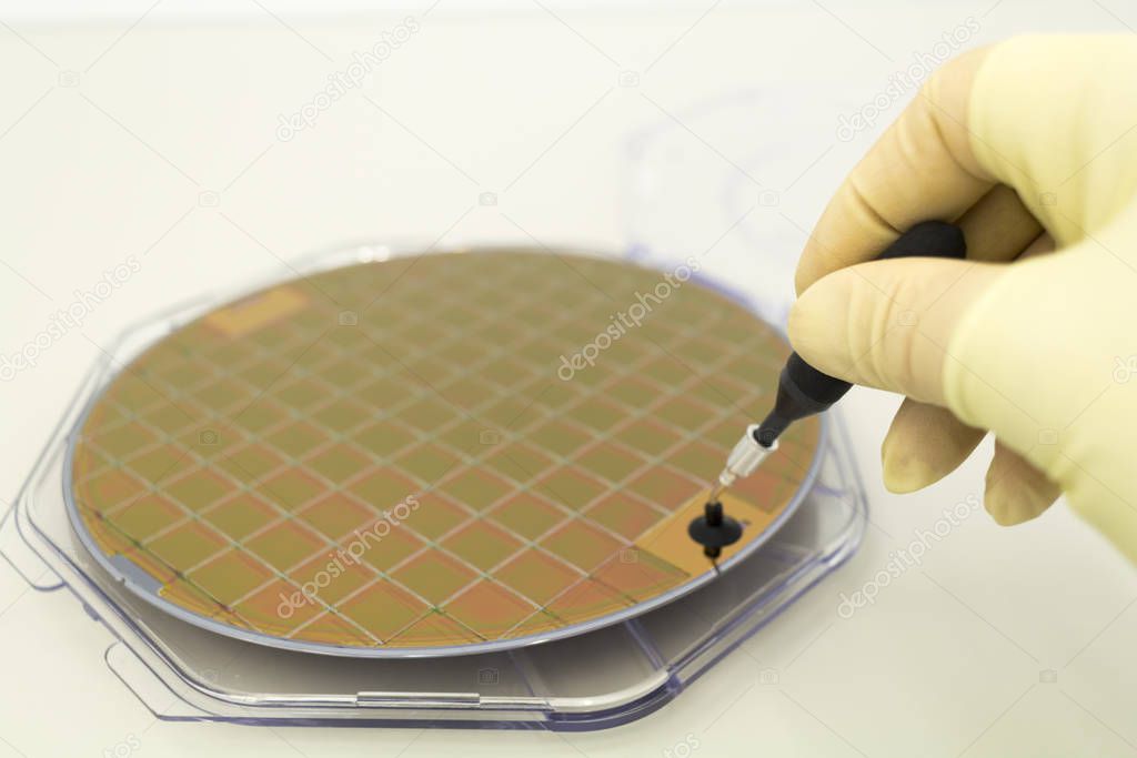 Silicone wafer in a plastic case on the table is take out by hand in a yellow glove and vacuum tweezers