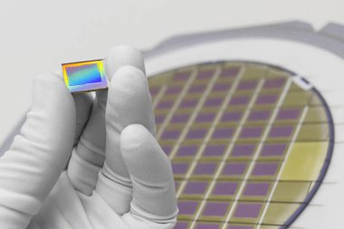 Hand in white glove holding microchip photo sensor matrix. On the background is diced silicon wafer with microchips. Focus on chip. clipart