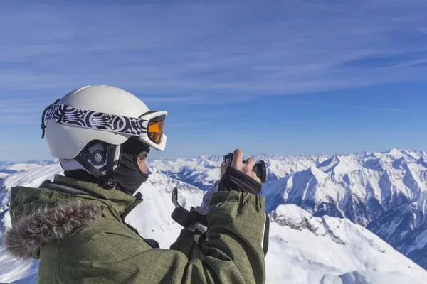 Skier άνθρωπος με πορτοκαλί γυαλιά σκι σε λευκό κράνος κάνουν φωτογράφηση στην κορυφή των Άλπεων βουνά. Στο φόντο των βουνών. Κλείσιμο προβολής. — Φωτογραφία Αρχείου