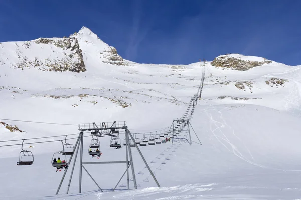 Sedia ascensore salire e funivia in primo piano sullo sfondo di montagne innevate e cielo azzurro.Alpi austriache in inverno . — Foto Stock