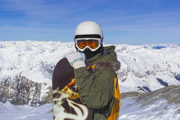 Beyaz kasklı turuncu kayak gözlüklü snowboardcu Alps dağlarının tepesinde poz veriyor. Dağların arka planında. — Stok fotoğraf