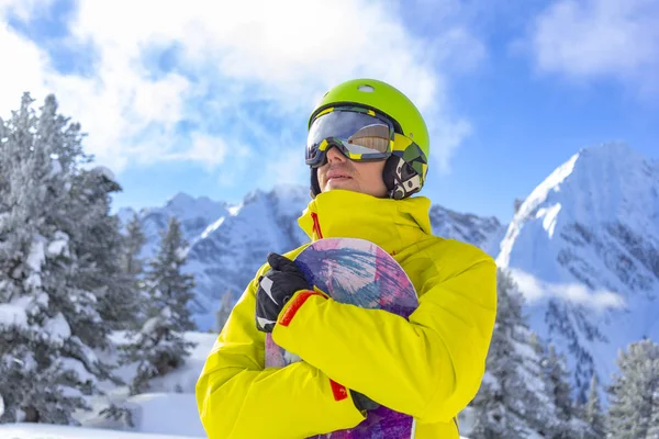 Snowboarder άνθρωπος με γυαλιά σκι σε πράσινο κράνος κάνουν φωτογράφηση στην κορυφή των Άλπεων βουνά. Στο φόντο των βουνών. Κλείσιμο προβολής. — Φωτογραφία Αρχείου