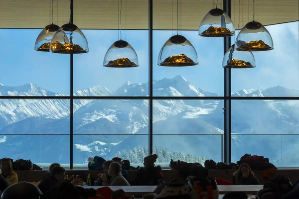 Austria Zillertal - 04 de febrero de 2019: Lámparas en forma de montaña cuelgan dentro de un restaurante frente a una ventana de montañas cubiertas de nieve en los Alpes austríacos. . —  Fotos de Stock