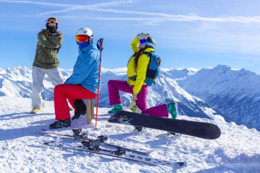 Üç mutlu arkadaş snowboardcular ve kayakçılar güneşli bir günde snowboard ve kayakla kayak pistinde eğleniyorlar..