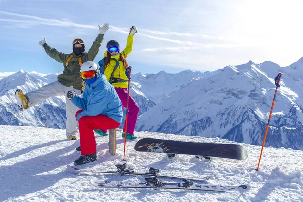 Τρεις χαρούμενοι φίλοι snowboarders και σκιέρ διασκεδάζουν στην πλαγιά του σκι με snowboards και σκι την ηλιόλουστη μέρα. — Φωτογραφία Αρχείου