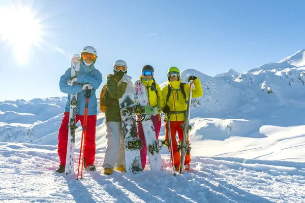 Τέσσερις χαρούμενοι φίλοι snowboarders και σκιέρ διασκεδάζουν στην πλαγιά του σκι με σκι και snowboards στην ηλιόλουστη μέρα. — Φωτογραφία Αρχείου