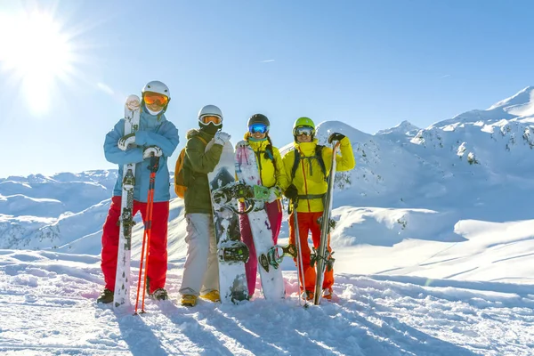 Vier vrolijke vrienden snowboarders en skiërs vermaken zich op de piste met ski en snowboards op zonnige dag. Rechtenvrije Stockafbeeldingen