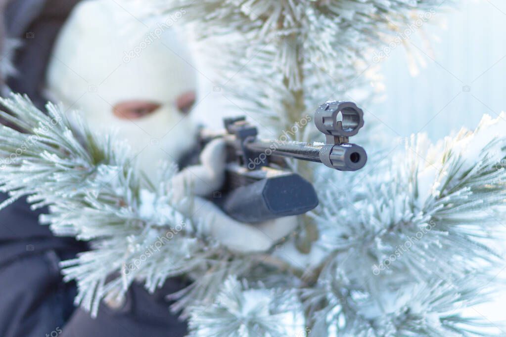 Masked man aims with rifle in winter forest.Focus on rifle.