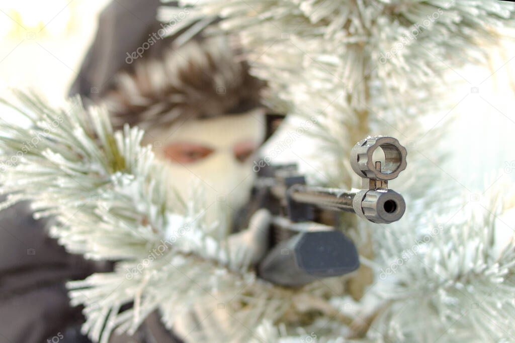 Masked man aims with rifle in winter forest.Focus on rifle.