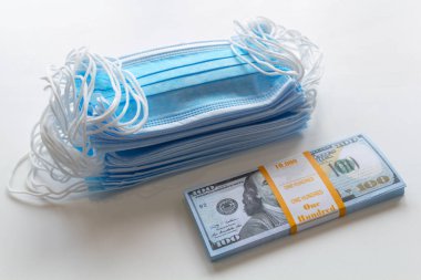 Bir paket tıbbi maske ve 100 dolarlık banknotlar daha yüksek fiyatların sembolü ve solunum yollarının virüslerden korunmasında bir eksiklik. Koruyucu maskelerin fiyatını arttırdı.