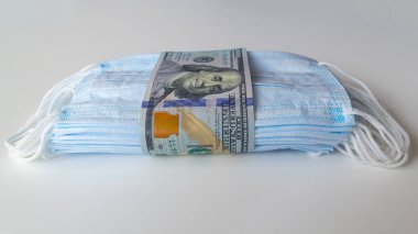 Daha yüksek fiyatların sembolü olarak 100 dolarlık banknotlara sarılı bir tıbbi maske paketi ve solunum yollarının virüslerden korunmasında bir eksiklik. Koruyucu maskelerin fiyatını arttırdı.