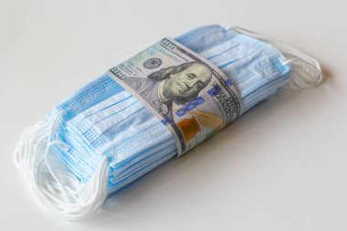 Daha yüksek fiyatların sembolü olarak 100 dolarlık banknotlara sarılı bir tıbbi maske paketi ve solunum yollarının virüslerden korunmasında bir eksiklik. Koruyucu maskelerin fiyatını arttırdı.
