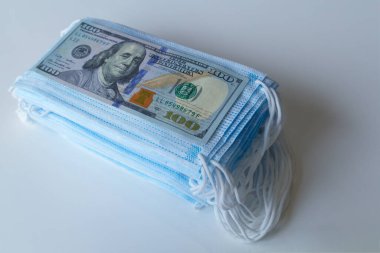 Bir paket tıbbi maske ve 100 dolarlık banknotlar daha yüksek fiyatların sembolü ve solunum yollarının virüslerden korunmasında bir eksiklik. Koruyucu maskelerin fiyatını arttırdı.