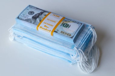 Bir paket tıbbi maske ve 100 dolarlık banknotlar daha yüksek fiyatların sembolü ve solunum yollarının virüslerden korunmasında bir eksiklik. Koruyucu maskelerin fiyatını arttırdı.
