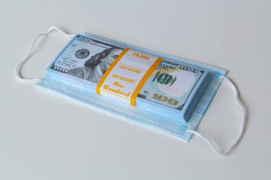 Bir tıbbi maske ve yüksek fiyatların sembolü olarak bir yığın 100 dolarlık banknot ve solunum yollarının virüslerden korunmasında bir eksiklik. Koruyucu maskelerin fiyatını arttırdı.