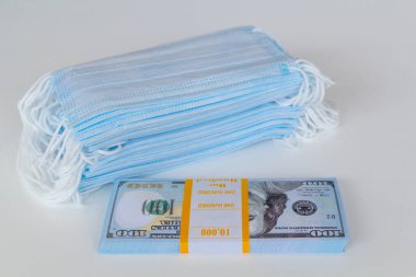 Bir paket tıbbi maske ve 100 dolarlık banknotlar daha yüksek fiyatların sembolü ve solunum yollarının virüslerden korunmasında bir eksiklik. Koruyucu maskelerin fiyatını arttırdı.