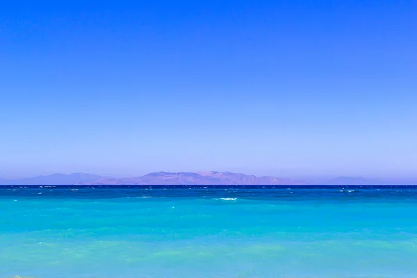 Simplemente paisaje con el color turquesa del mar, las montañas en el horizonte y el cielo azul degradado.Horizonte línea entre el mar Mediterráneo tranquilo y el cielo azul claro — Foto de Stock