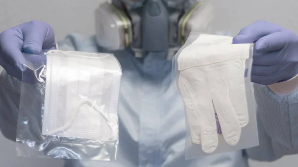 A man in a protective suit demonstrates and offers a medical mask and gloves for personal protection against viruses - health and medicine concept.