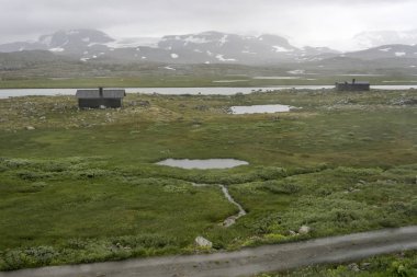 Finse yakınlarında, alçak bulutların altında, dağ gölündeki izole evler.