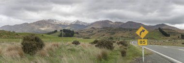 Tepeler arasında bükülmekte olan 94 nolu yol, Red Tussock otlarıyla kaplı, Central Hill, Southland, Güney Adası, Yeni Zelanda yakınlarındaki parlak bulutlu bahar ışığı altında çekiliyor.